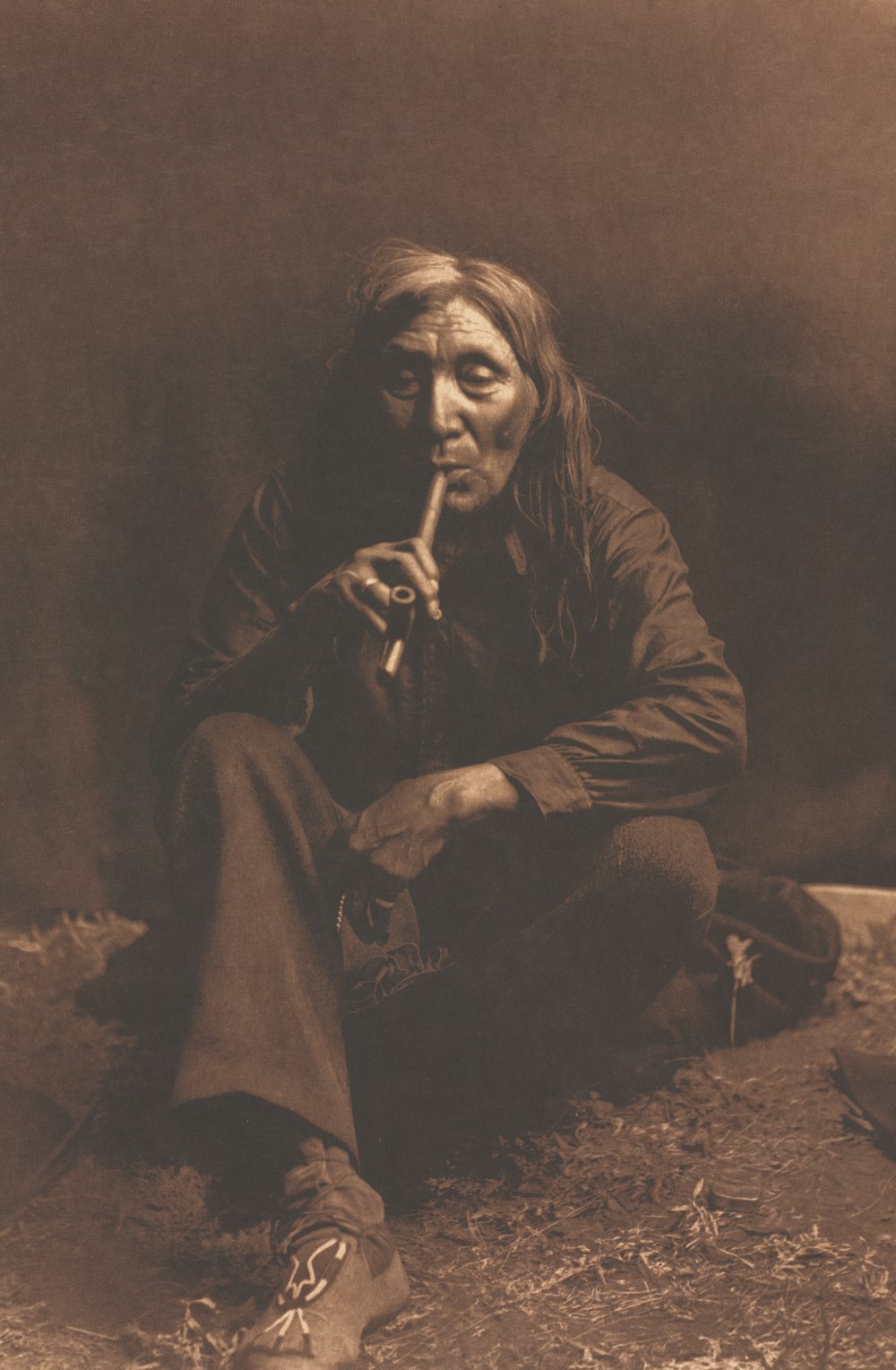an old photo of a native american man smoking a pipe