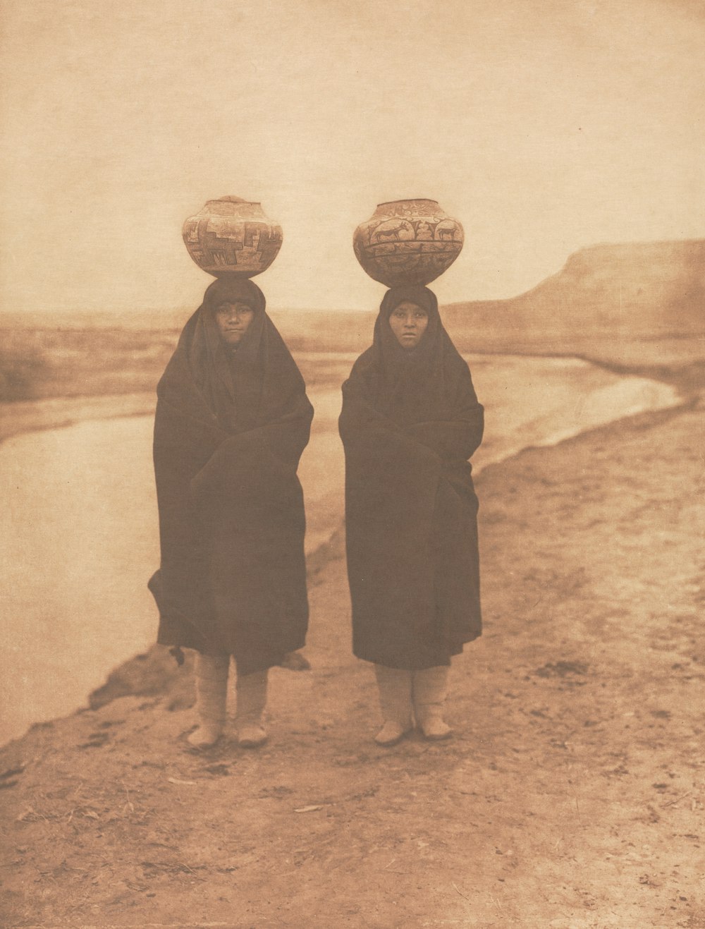 two women with baskets on their heads standing on a hill