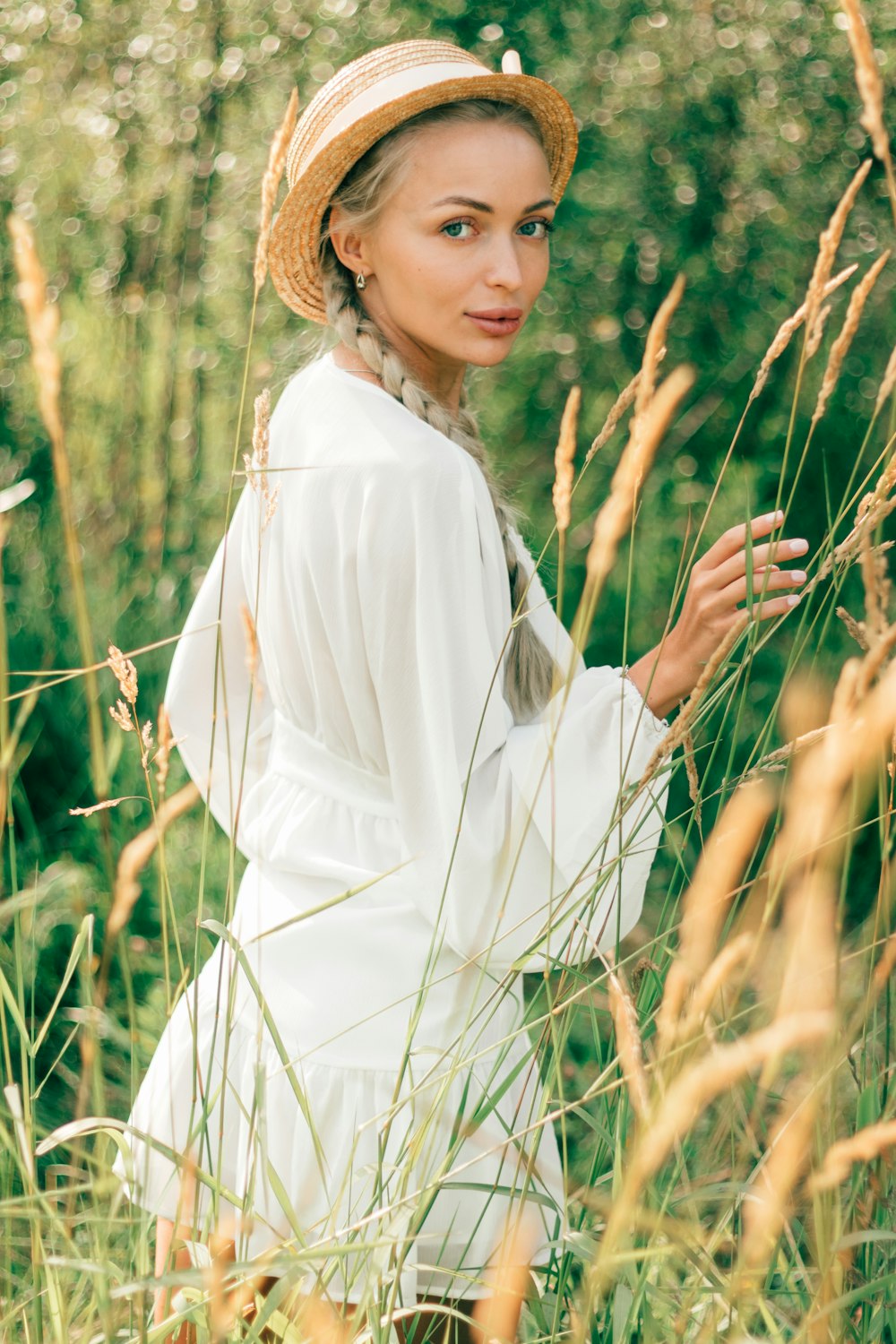 a woman in a white dress and straw hat standing in tall grass