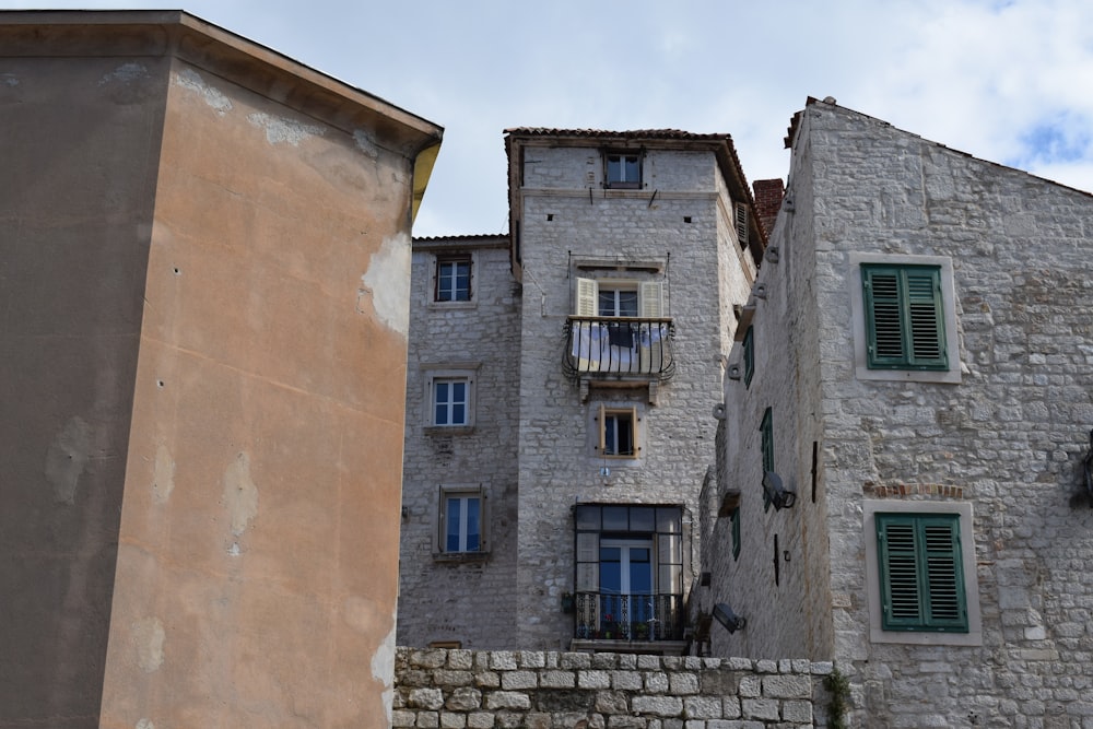 a stone building with green shutters next to a stone wall