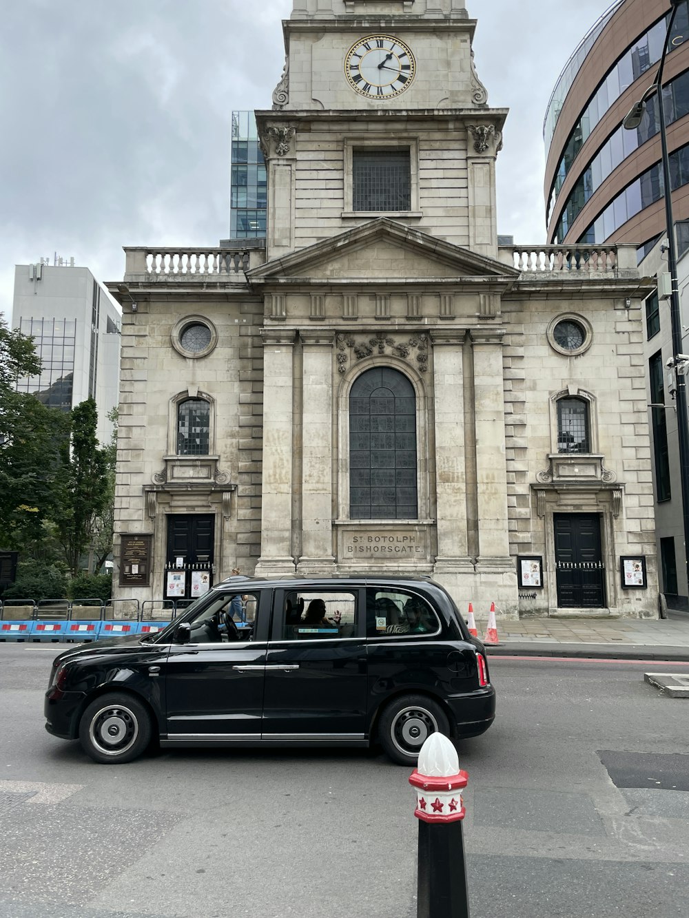 a black car driving past a tall building with a clock tower