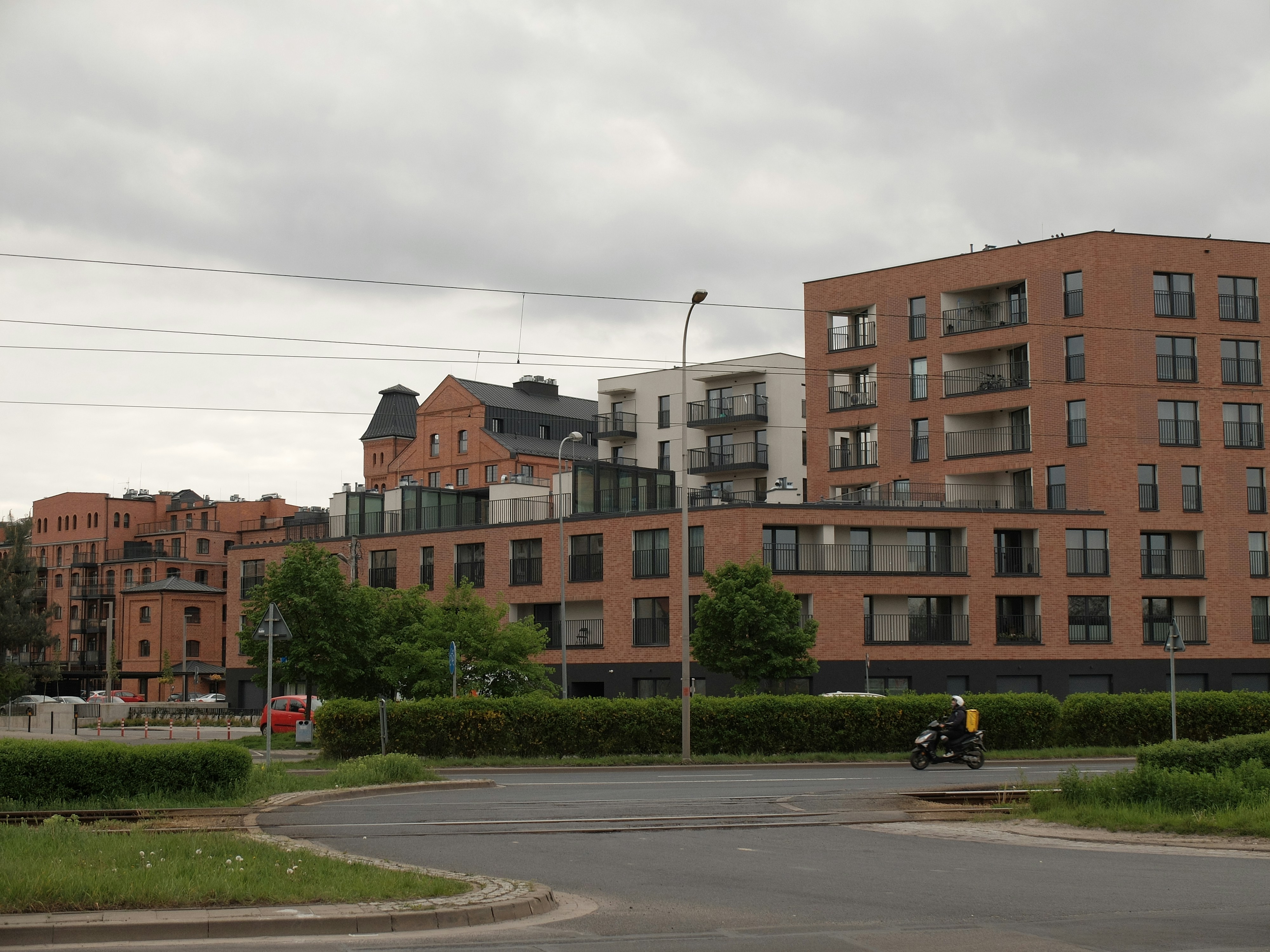 a motorcyclist rides down a street in front of a row of brick