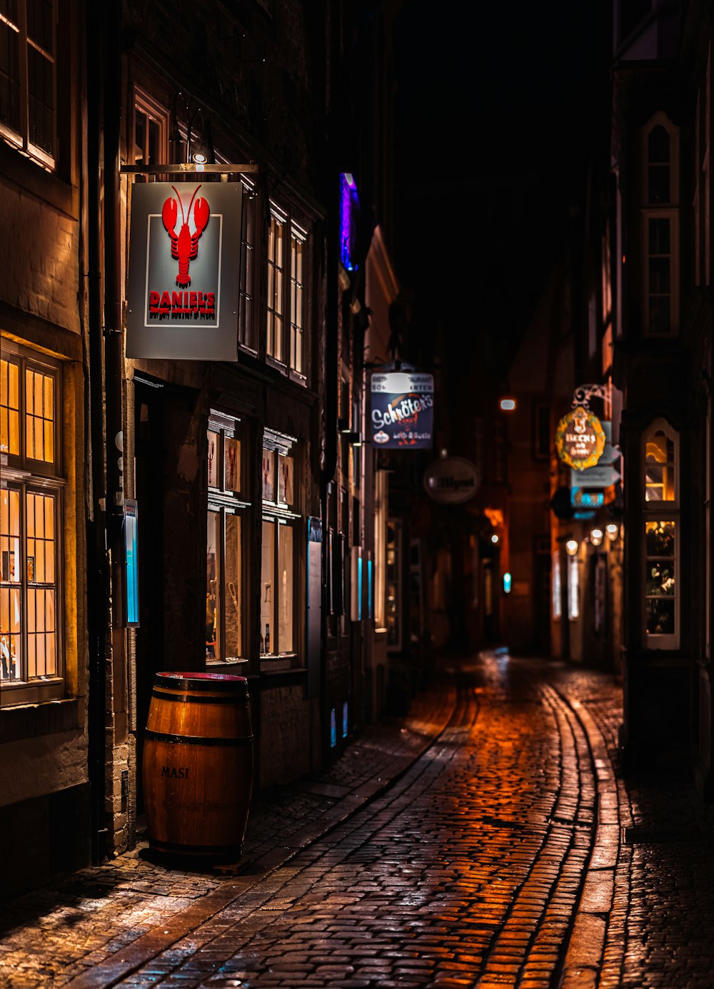 a cobblestone street at night with a barrel in the foreground