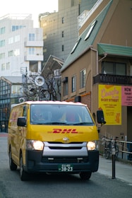 a yellow dhl van driving down a city street with cla 250 tyres for delivery