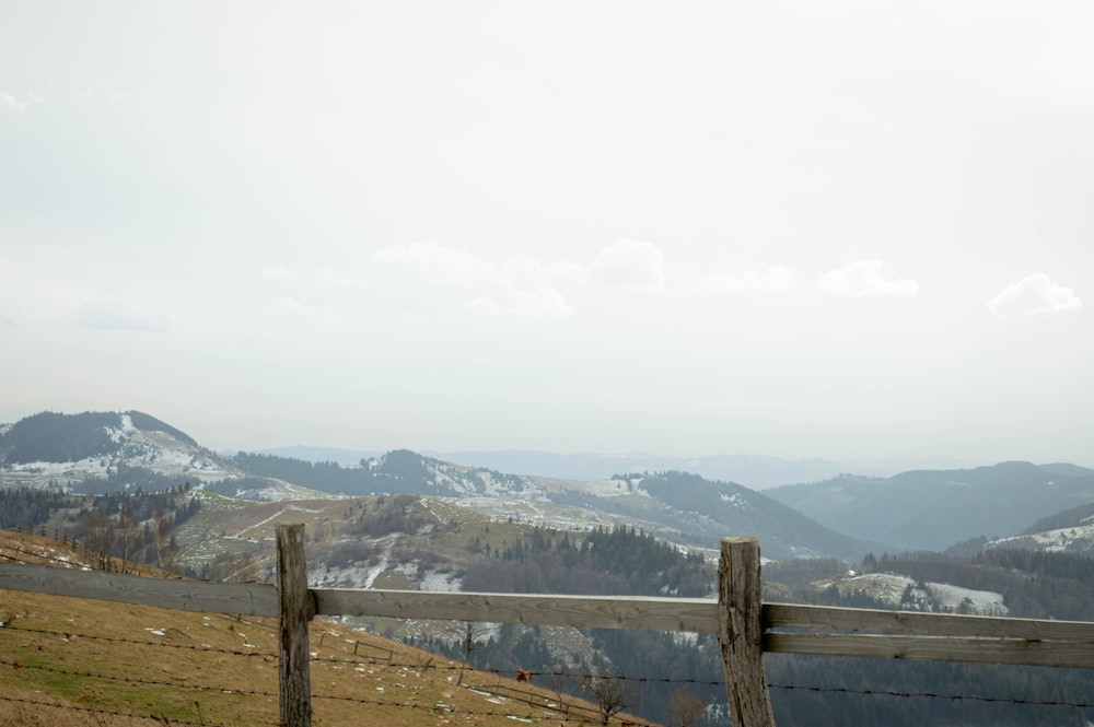 a wooden fence on top of a hill with mountains in the background