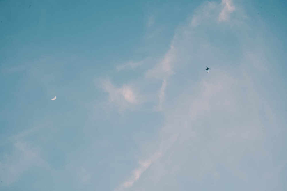 a plane flying in the sky with a half moon in the background