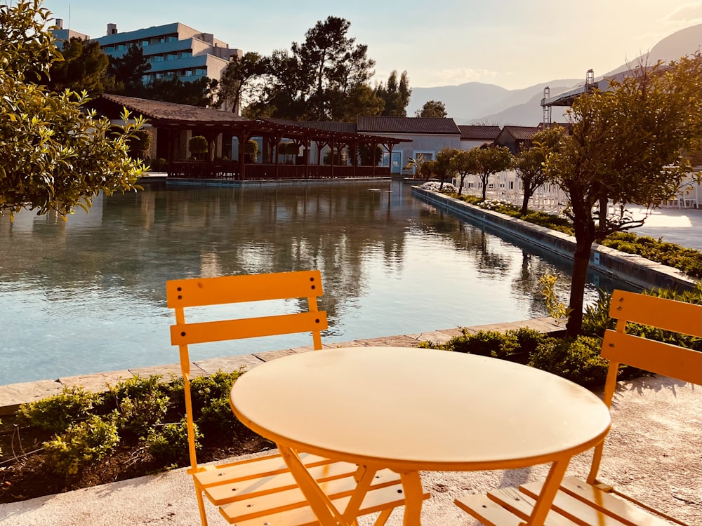 two yellow chairs and a white table near a lake