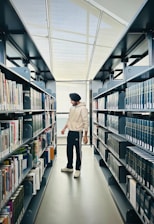 a man walking down a long aisle in a library