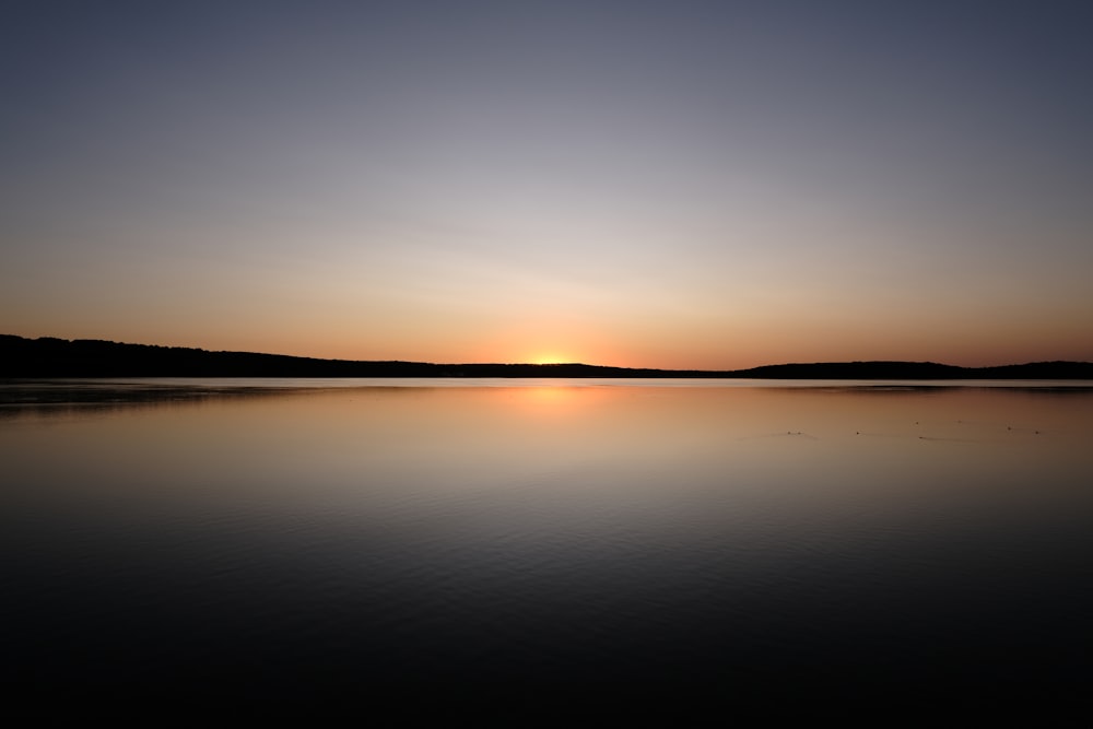 the sun is setting over a calm lake