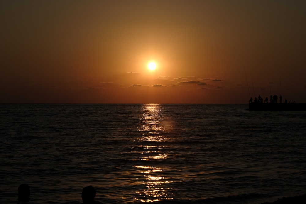 the sun is setting over the ocean with a boat in the distance