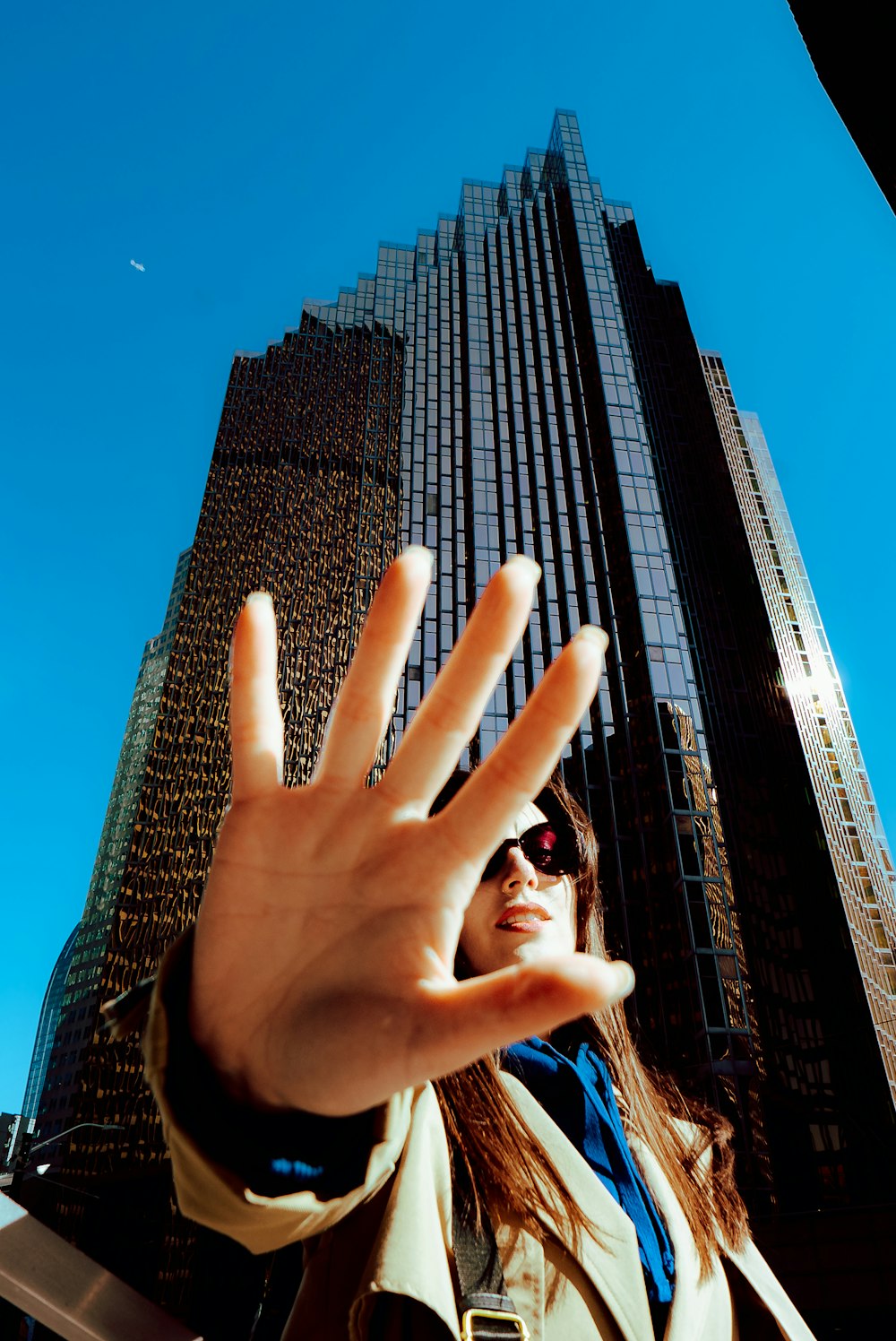a woman making a hand gesture in front of a tall building