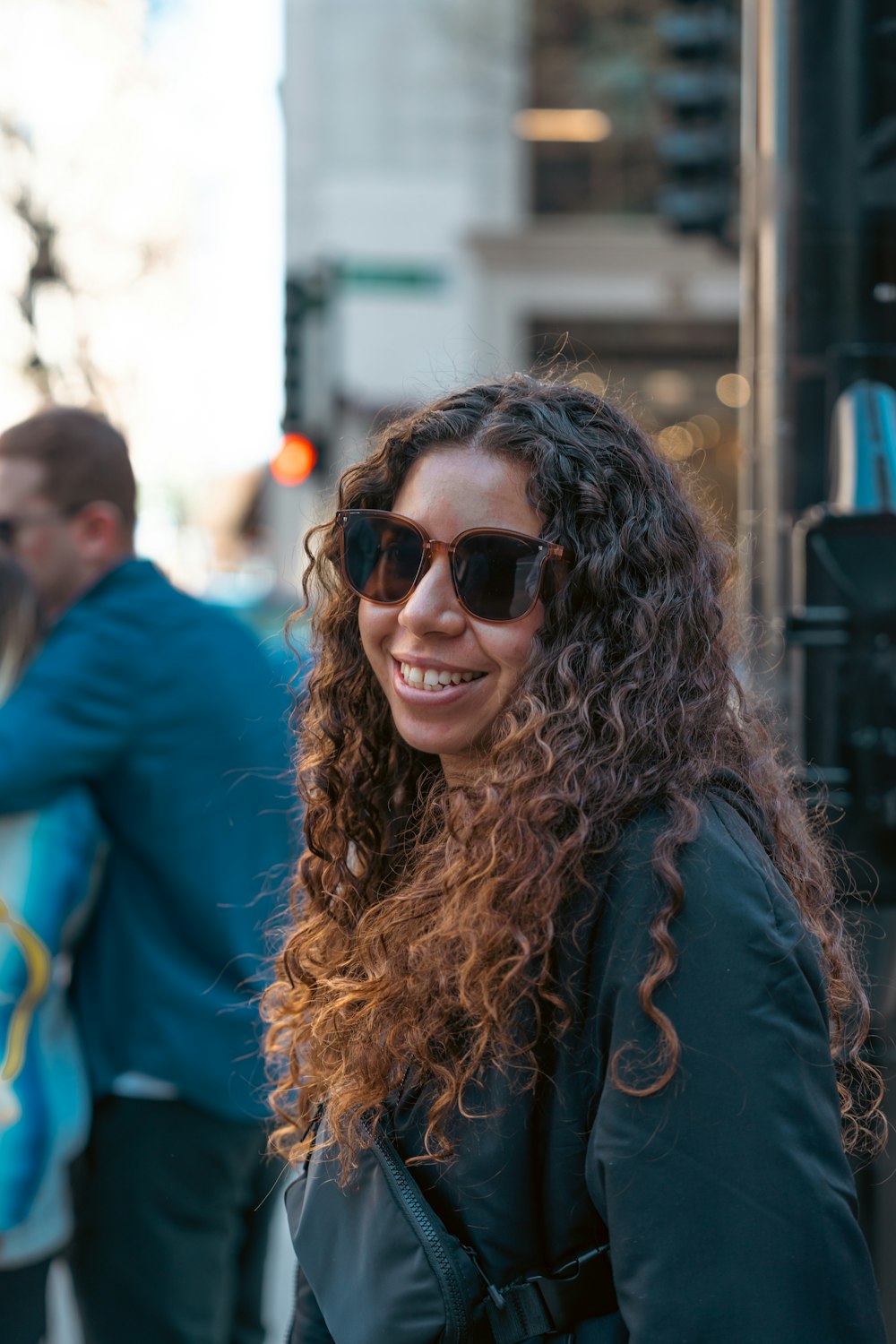 a woman with curly hair and sunglasses standing on the street