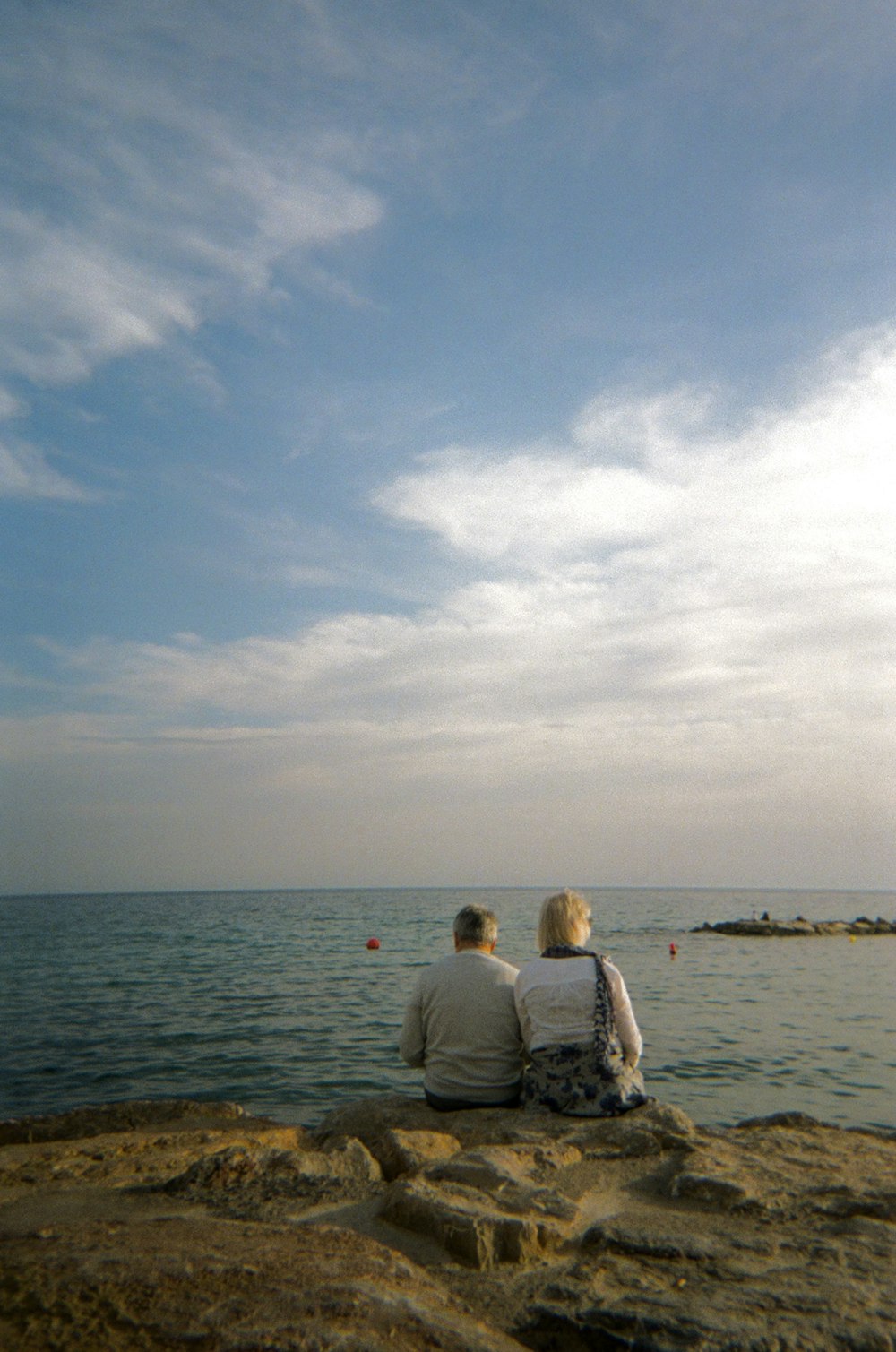 a man and a woman sitting on a rock looking out at the ocean