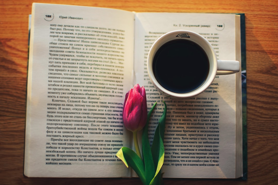 Strong tasty aromatic coffee on the window with an interesting book and pink tulip top view. The morning sun shines on a book and fragrant coffee, and beautiful fresh pink tulips lie nearby