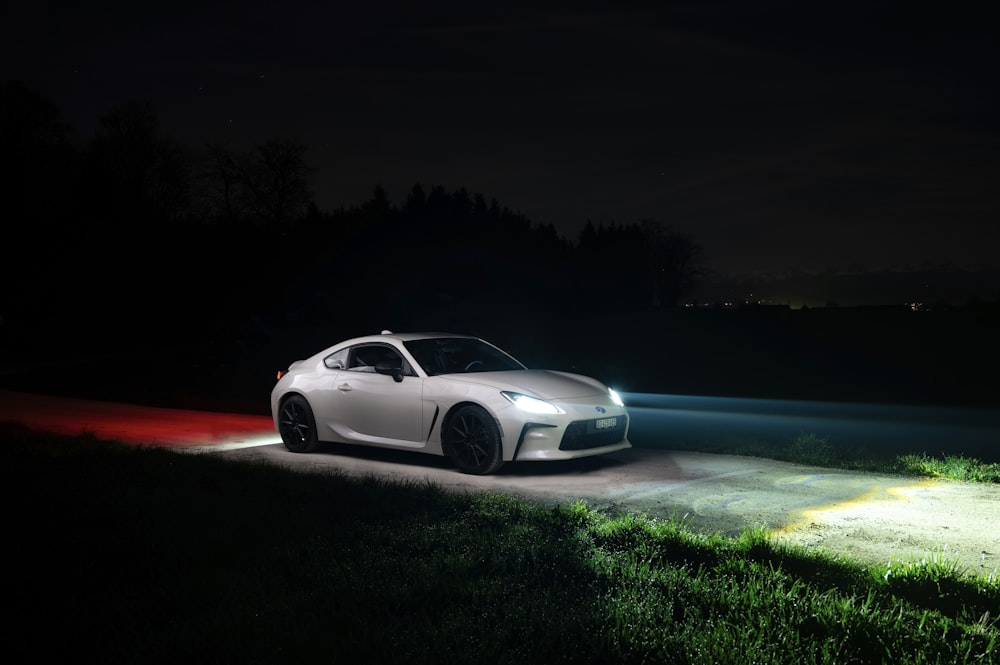 a white sports car driving down a road at night