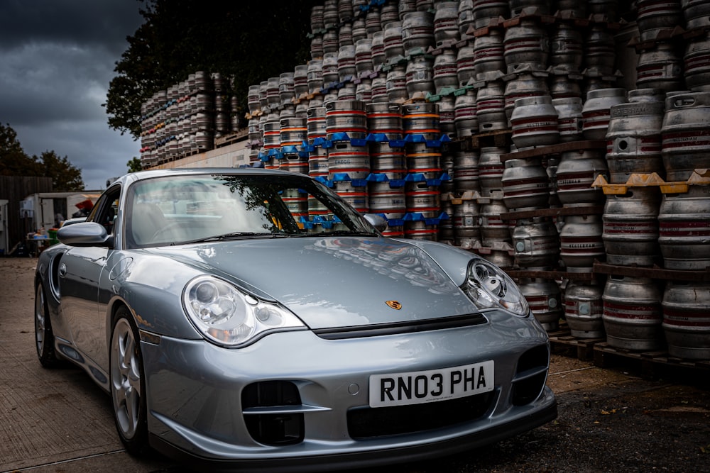 a silver sports car parked in front of stacks of barrels