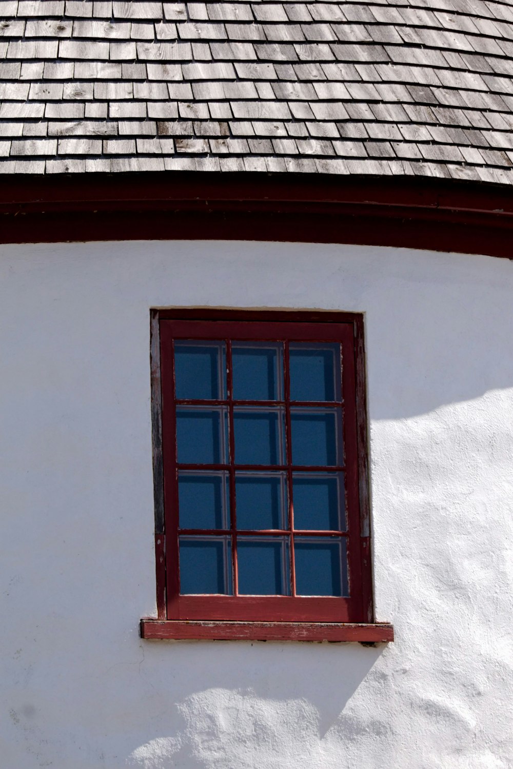 a white building with a red window and tiled roof