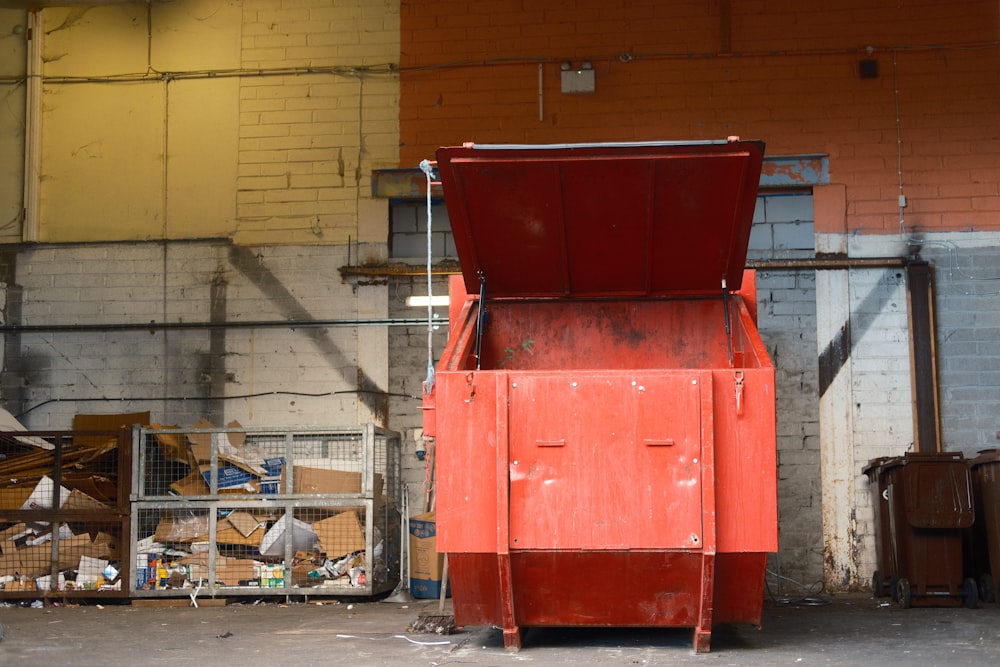 a red trash can sitting in front of a brick wall