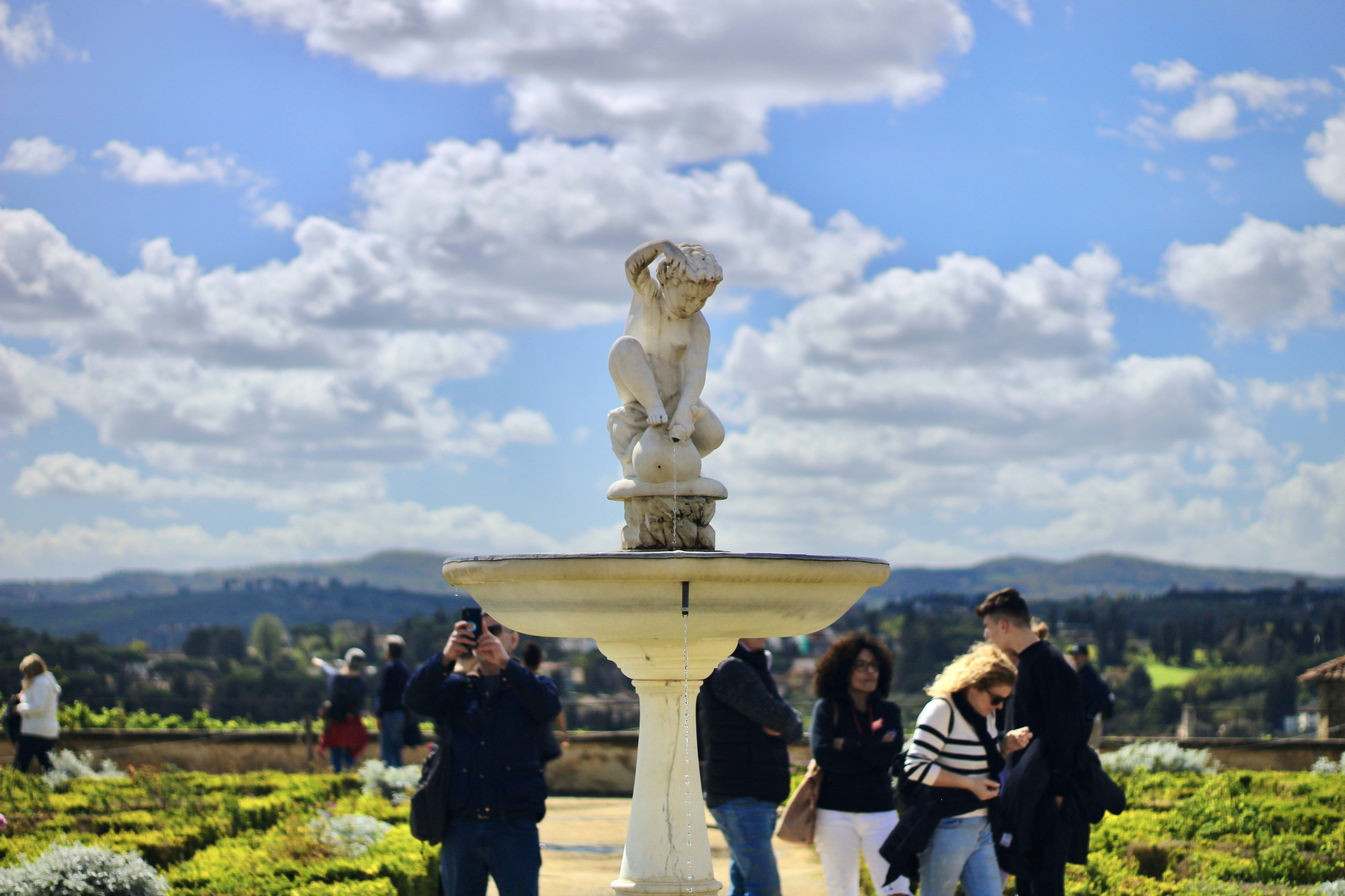 a group of people standing around a fountain, 