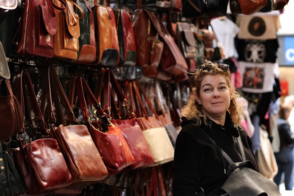 a woman standing in front of a wall of purses