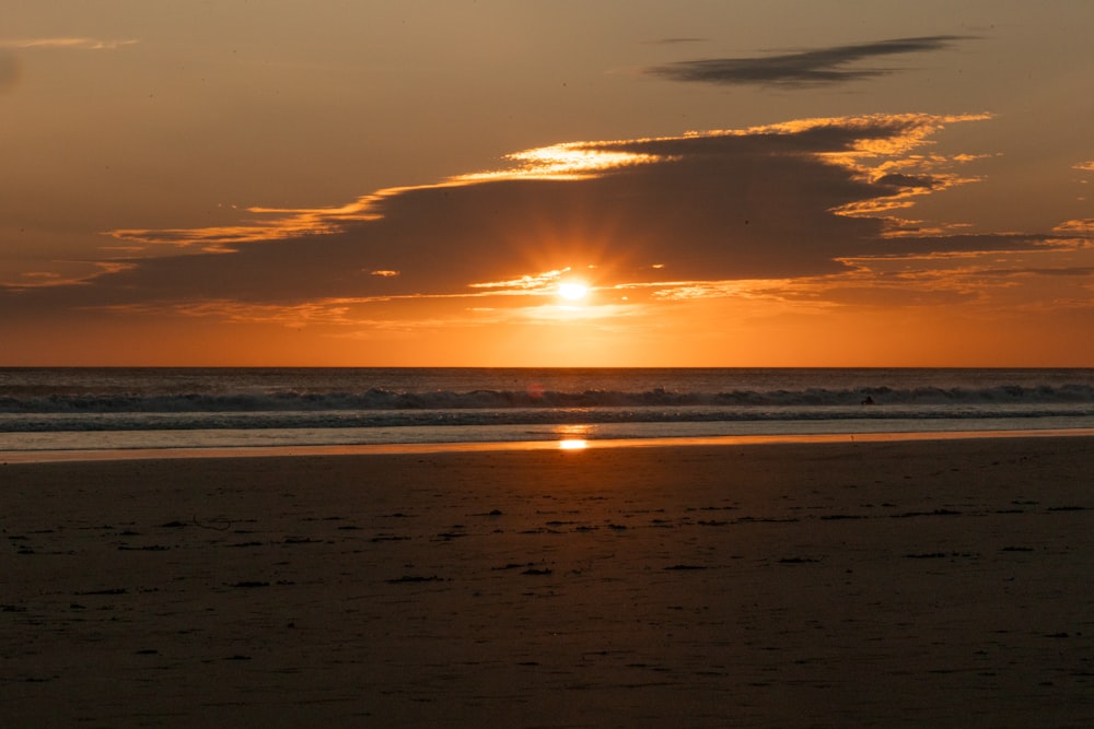 the sun is setting over the ocean on the beach