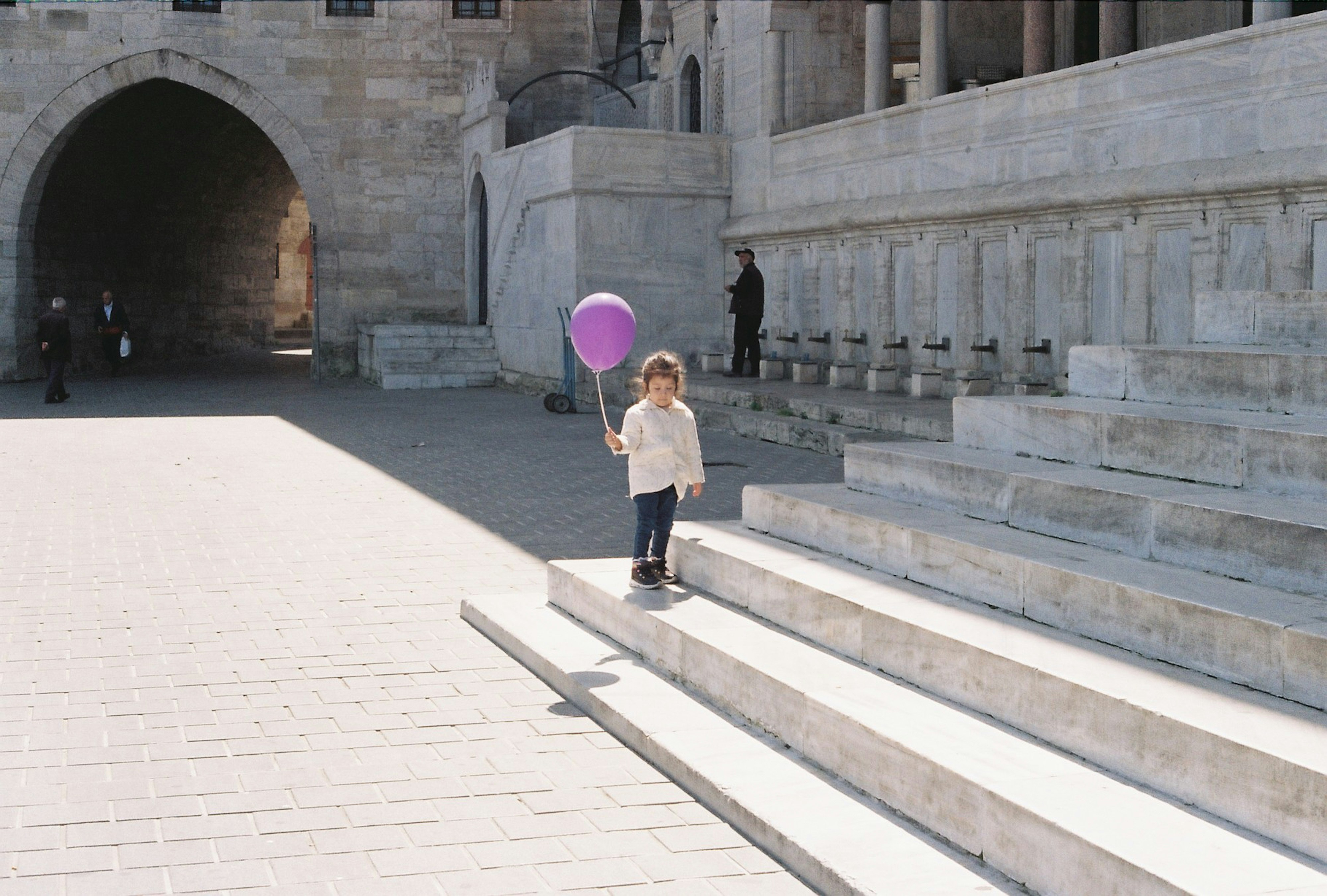 a little girl holding a purple balloon standing on some steps