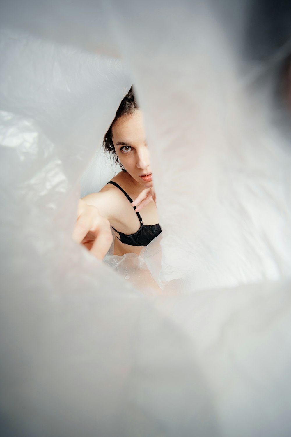 a woman in a black bra looking through a hole in a sheet