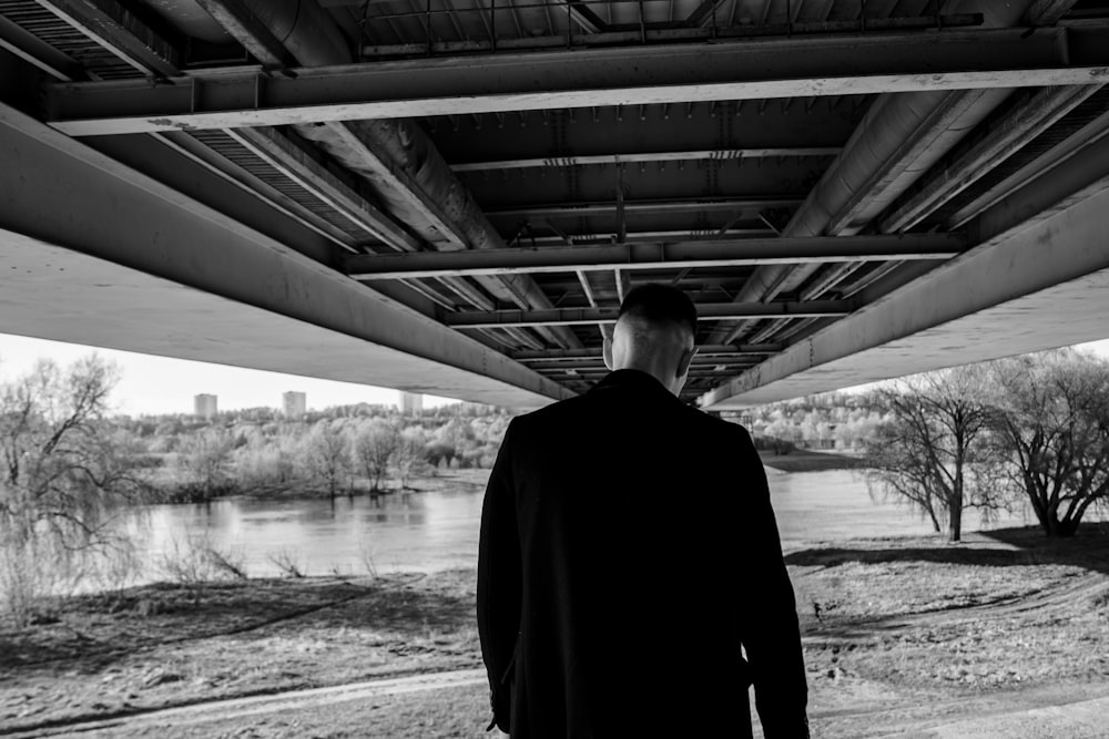 um homem parado debaixo de uma ponte ao lado de um rio