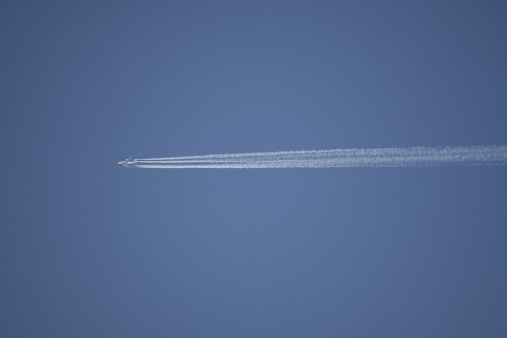 a jet flying through a blue sky leaving a trail of smoke