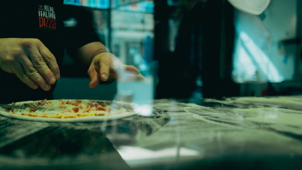 a person putting toppings on a pizza on a plate