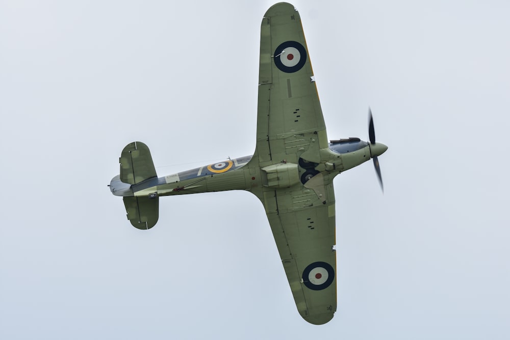 un avión verde volando en el cielo con una hélice