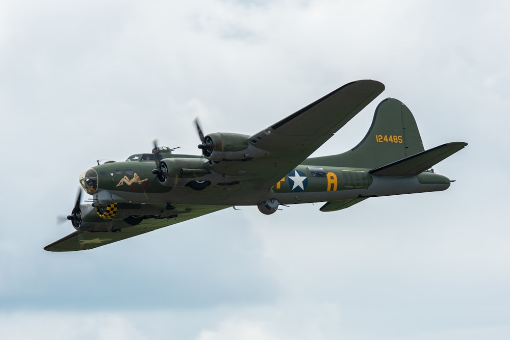 a green airplane flying through a cloudy sky