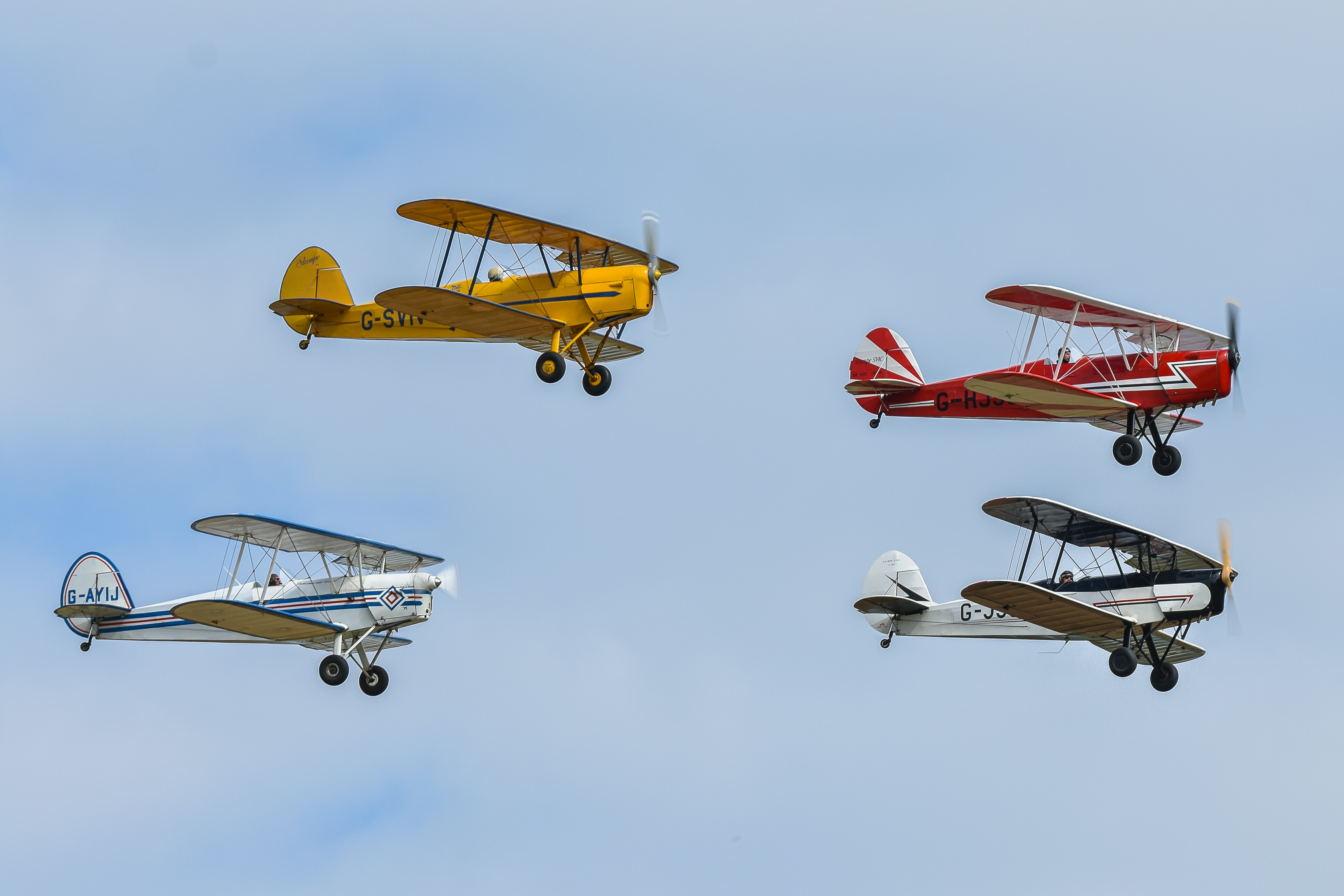 a group of four small airplanes flying through a blue sky, Four Stampe SV4C