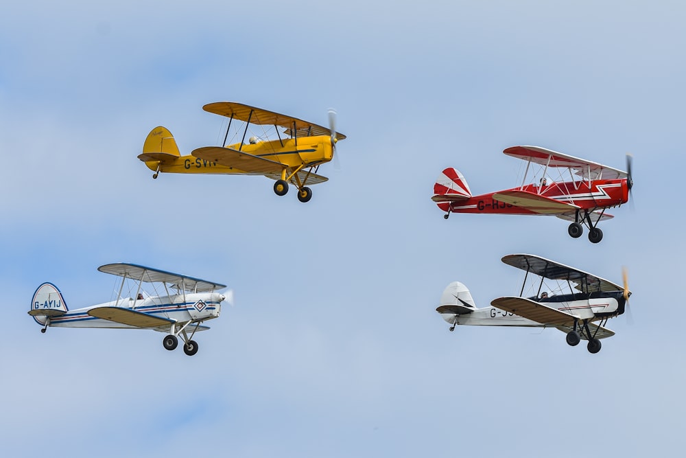 a group of four small airplanes flying through a blue sky