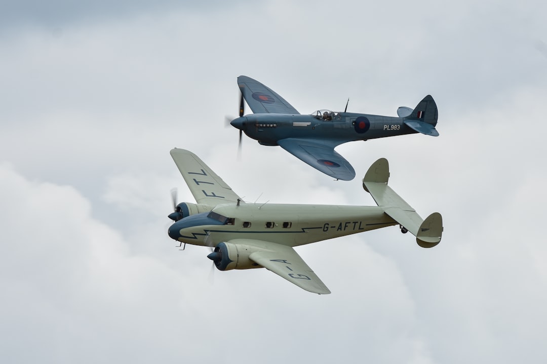 two planes flying in the sky on a cloudy day, A Lockheed 12A Electra Junior flying with a Supermarine Spitfire