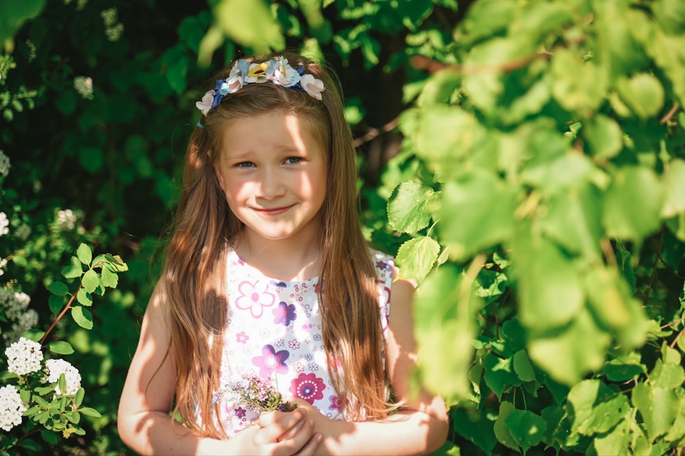 a little girl standing in front of a bush