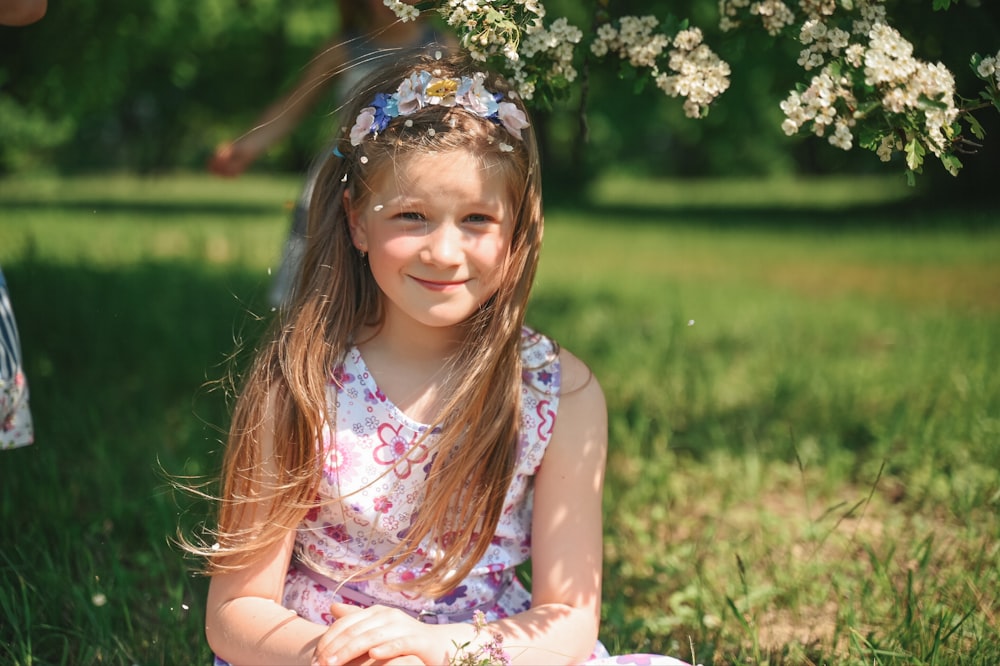 a little girl sitting in the grass with a flower in her hair