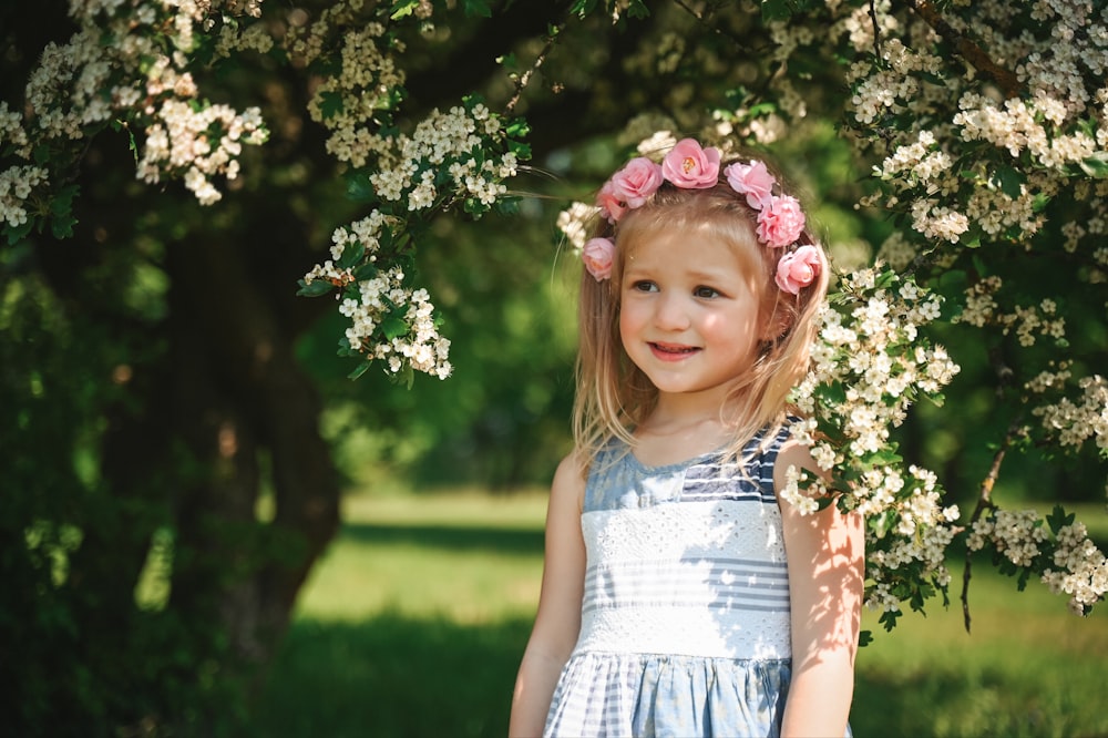 a little girl standing under a tree with flowers in her hair