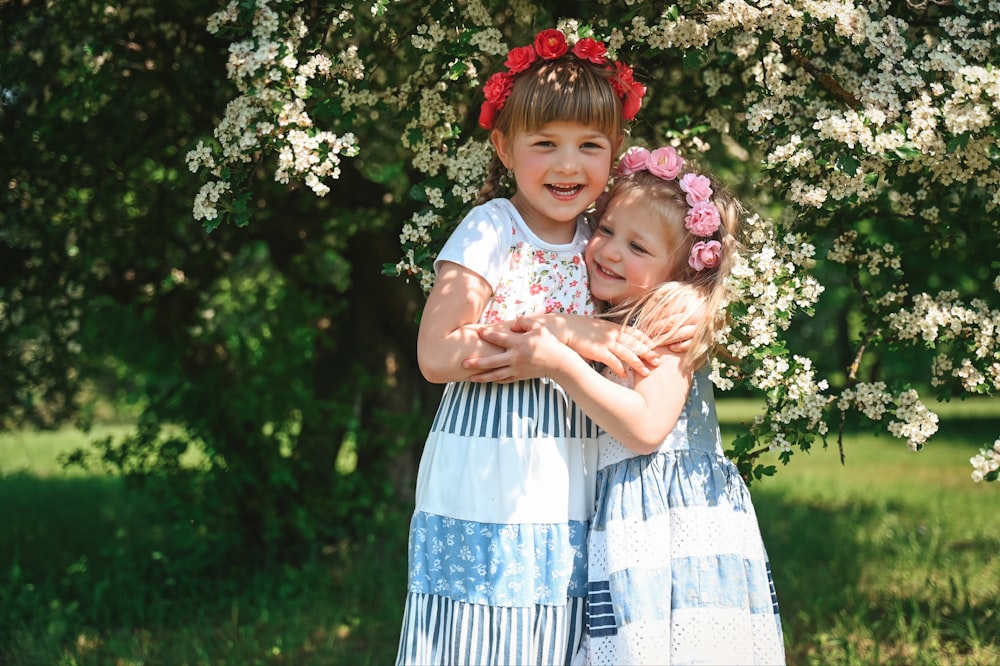 two little girls hugging each other in front of a tree