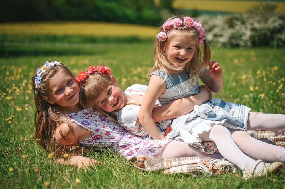 three little girls sitting on a blanket in a field
