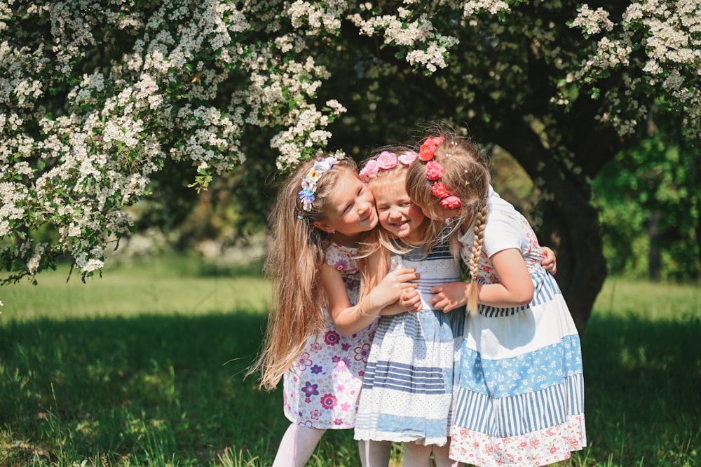 three little girls standing in front of a tree