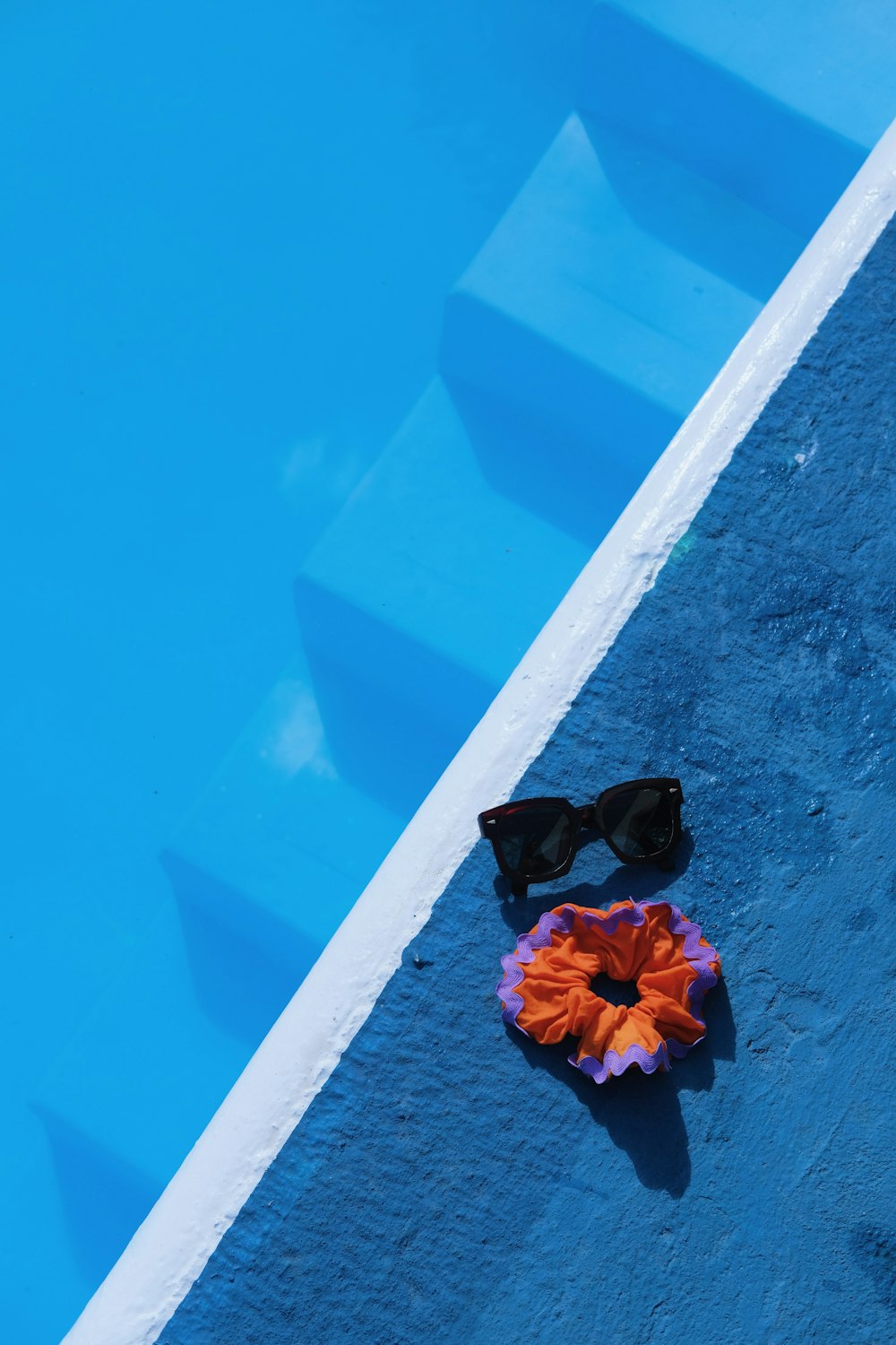 a pair of sunglasses and a flower on the edge of a pool