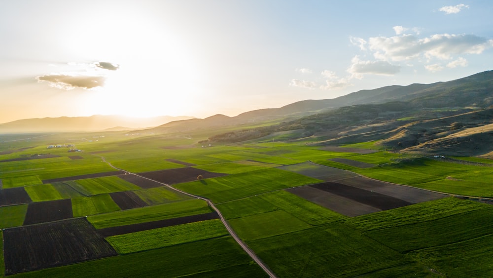 an aerial view of a green field with mountains in the background