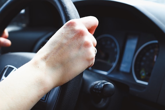 a person driving a car with their hand on the steering wheel