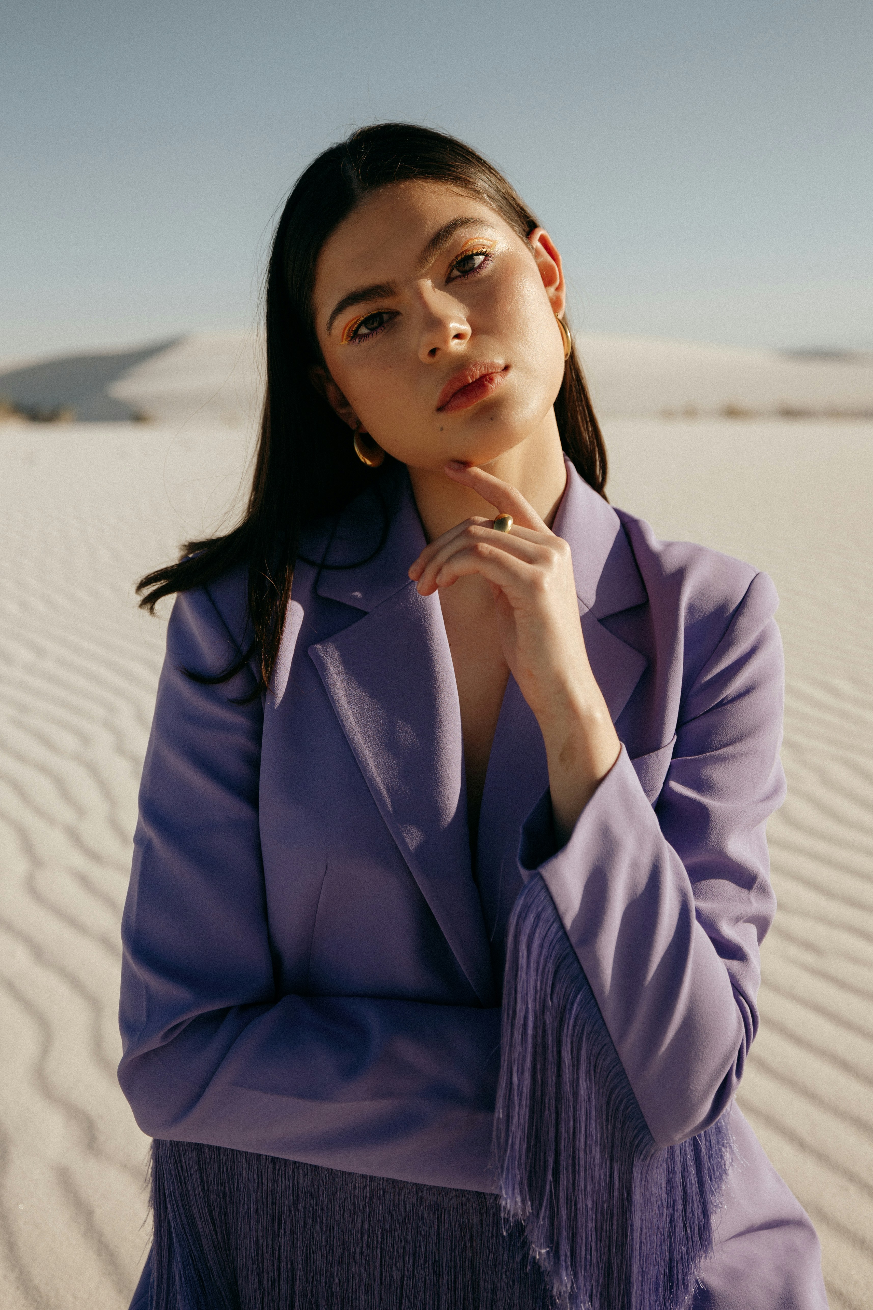 a woman sitting in the sand with her hand on her chin