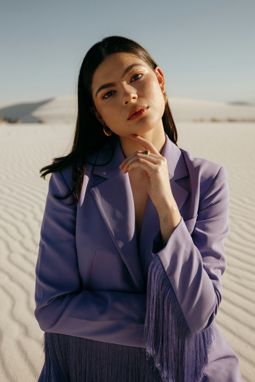 a woman sitting in the sand with her hand on her chin