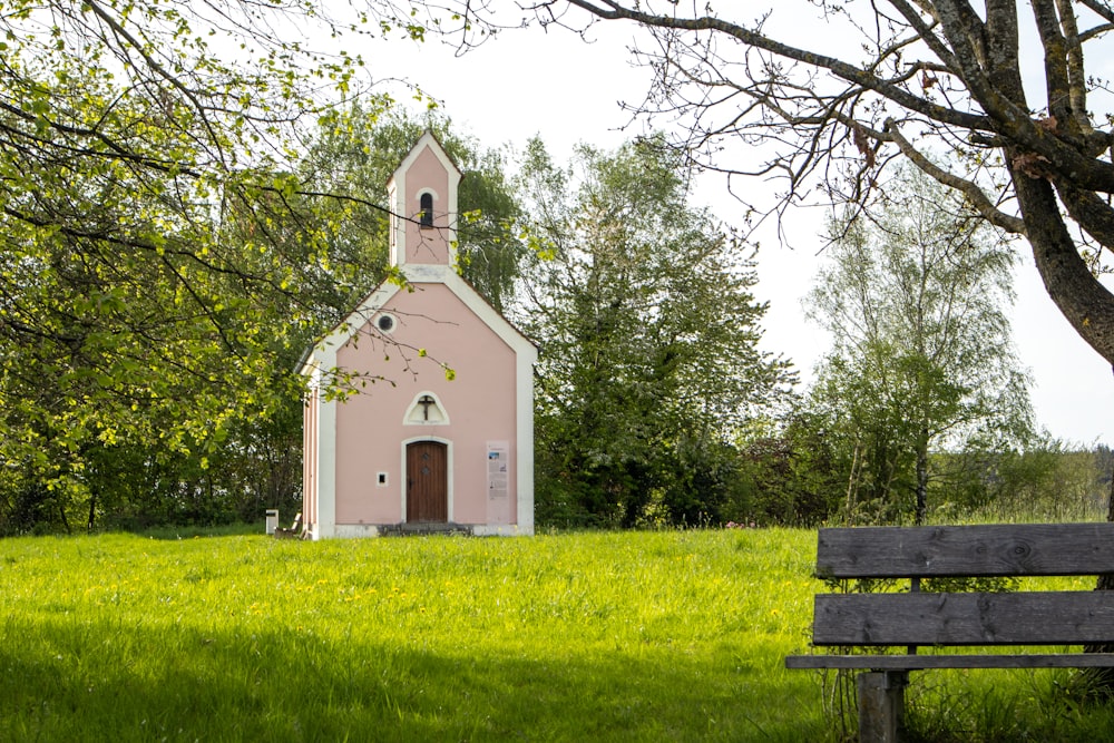 a small pink church in the middle of a green field