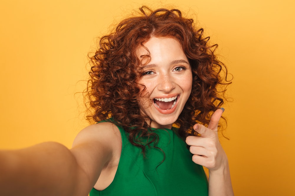 a woman with curly red hair is smiling and pointing to the camera