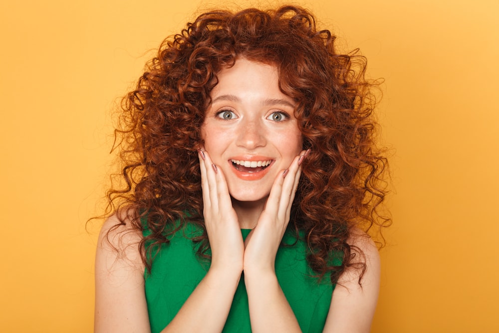 a woman with red curly hair smiling and holding her hands to her face