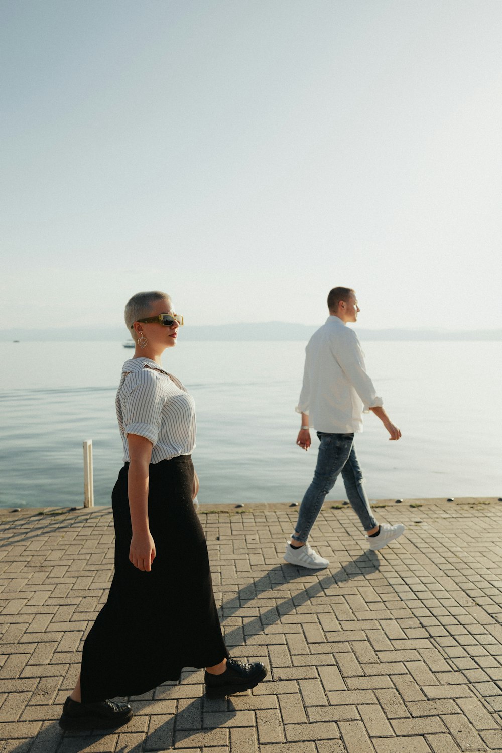 a man and a woman walking on a brick walkway near the water